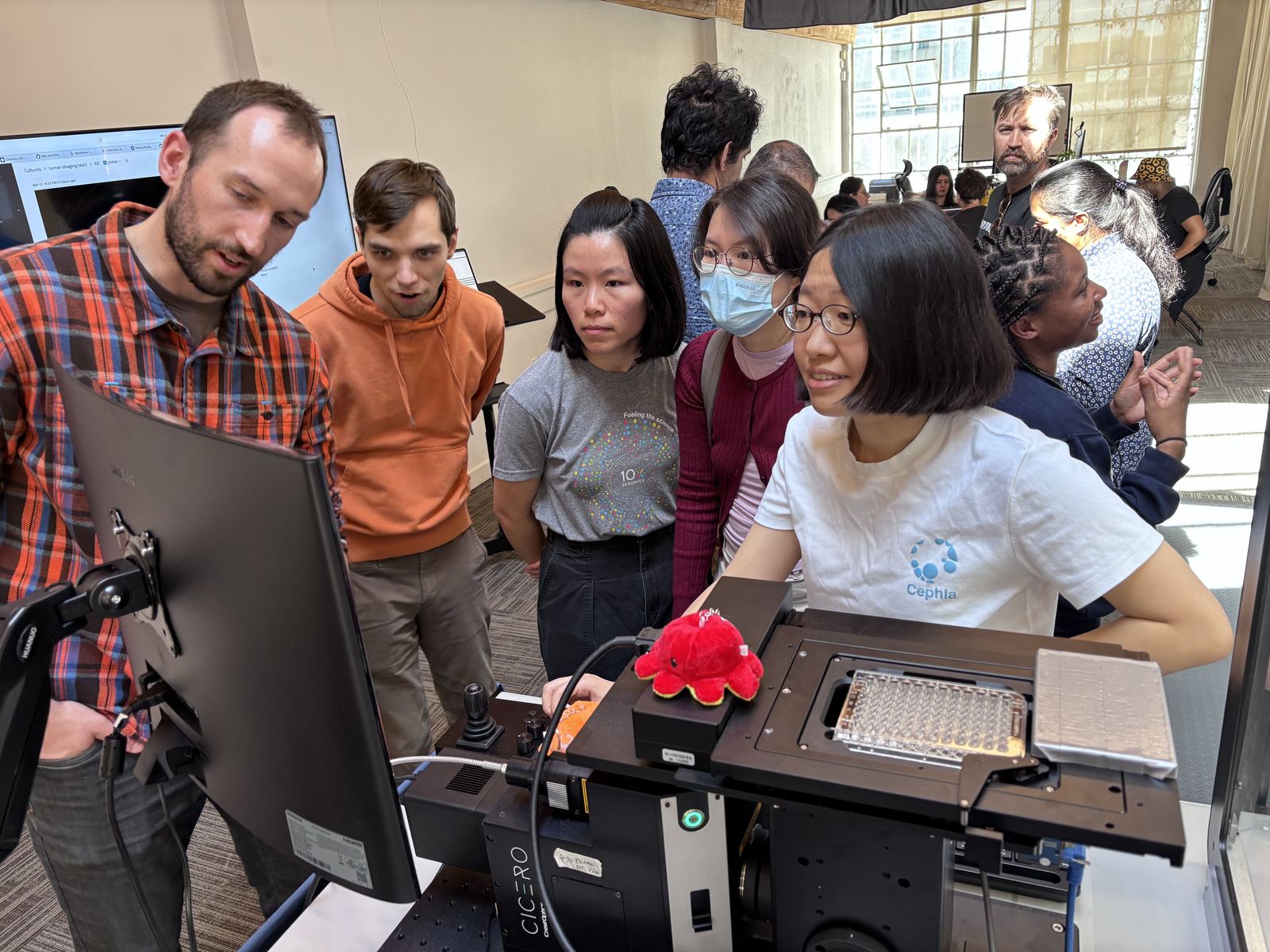 A team gathered around a lab instrument and monitor, watching a run.