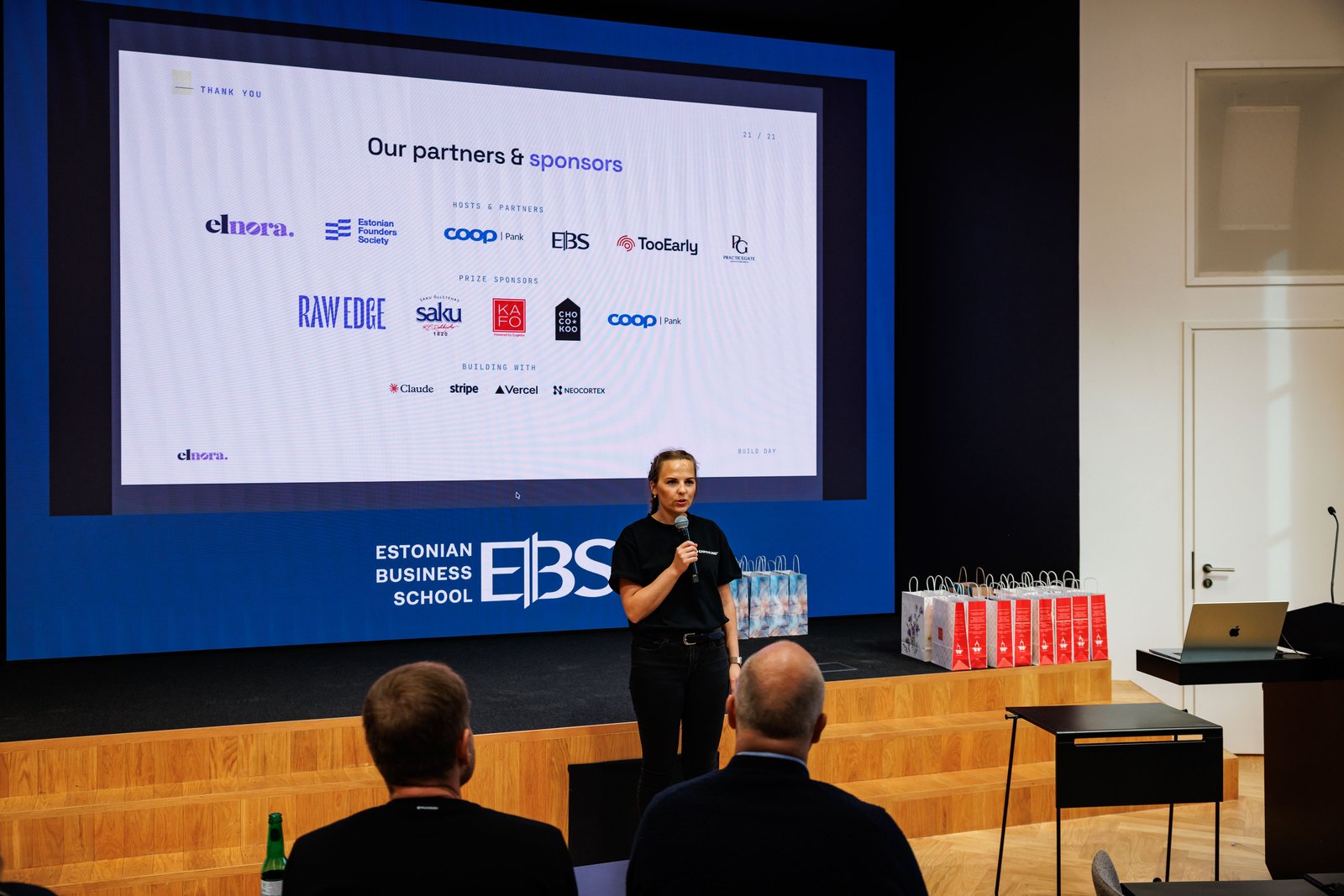 A host closing Build Day on stage, with prize bags lined up beside the lectern.