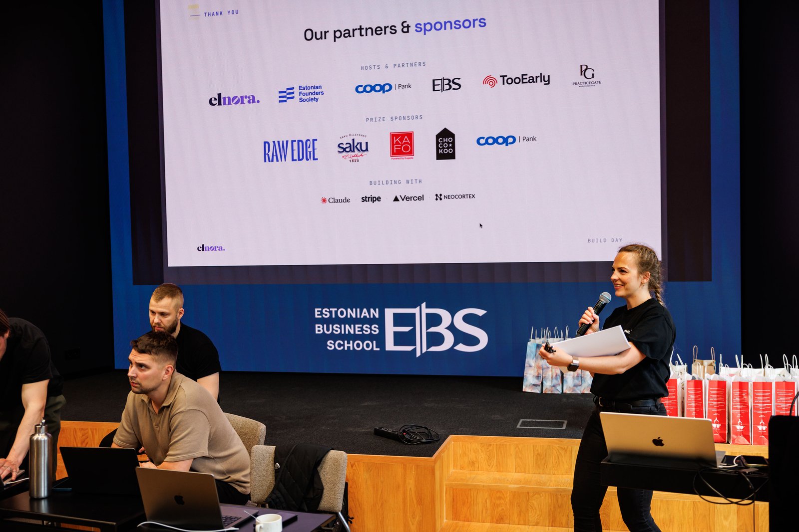 The partners and sponsors slide on the Estonian Business School screen, with a host at the microphone beside it.