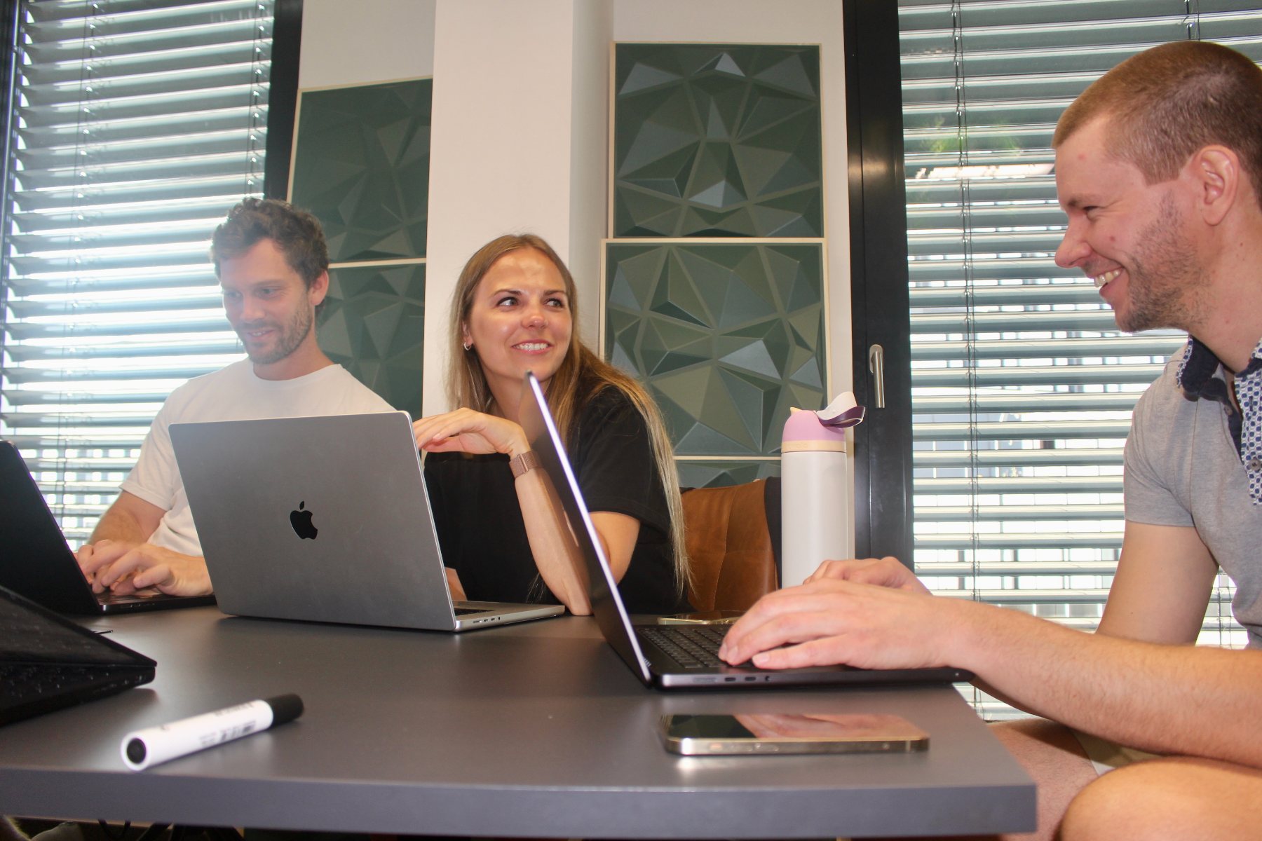 The Elnora and UniteLabs teams laughing together around a table of laptops in the Munich office.
