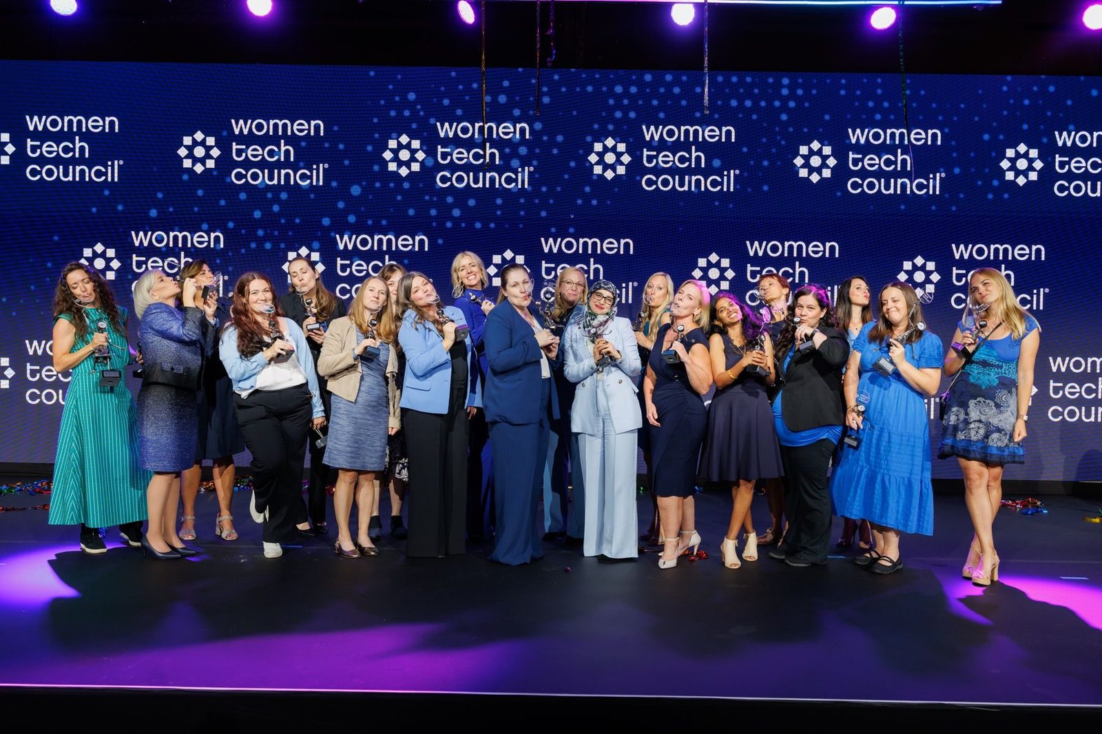 A group of 2026 honorees, Carmen Kivisild among them, posing with their trophies in front of the Women Tech Council backdrop.