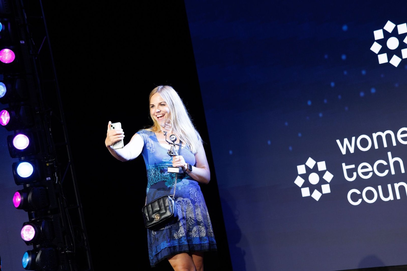 Carmen Kivisild taking a selfie on stage with her trophy beside the Women Tech Council logo.